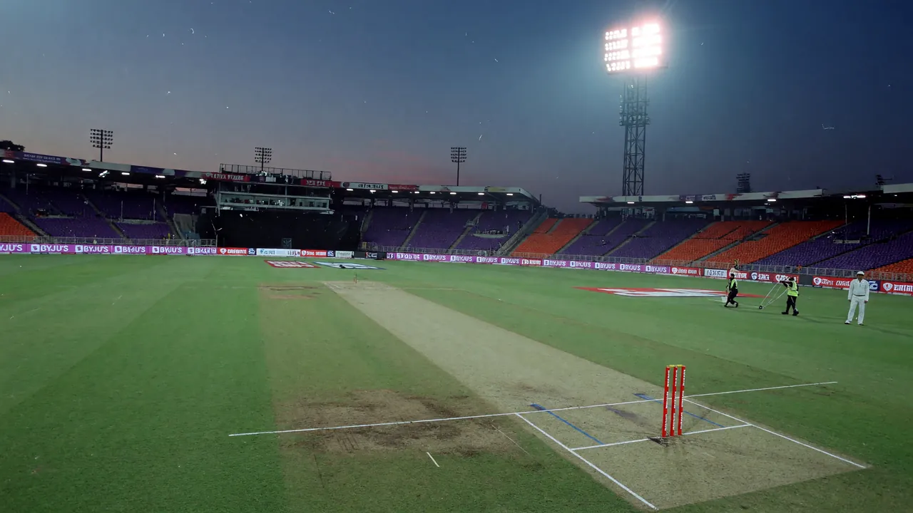 Editorial photograph of a quiet T20 pitch under cool evening floodlights, no players in frame — referral illustration card.