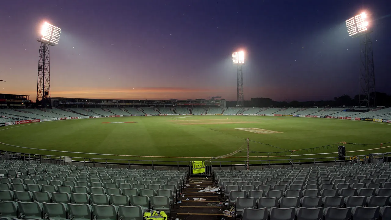 Floodlit cricket pitch at dusk with empty foreground.